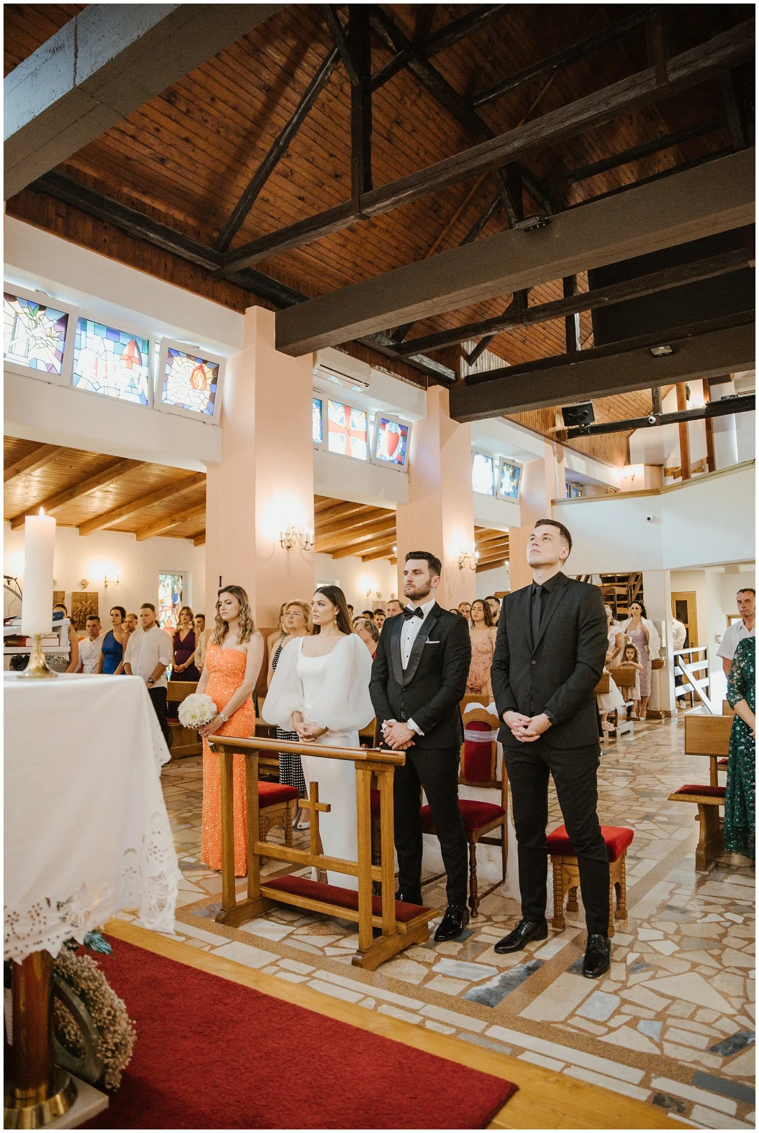 Mladenci i kumovi stoje ispred oltara u crkvi, okruženi gostima tijekom vjenčane ceremonije