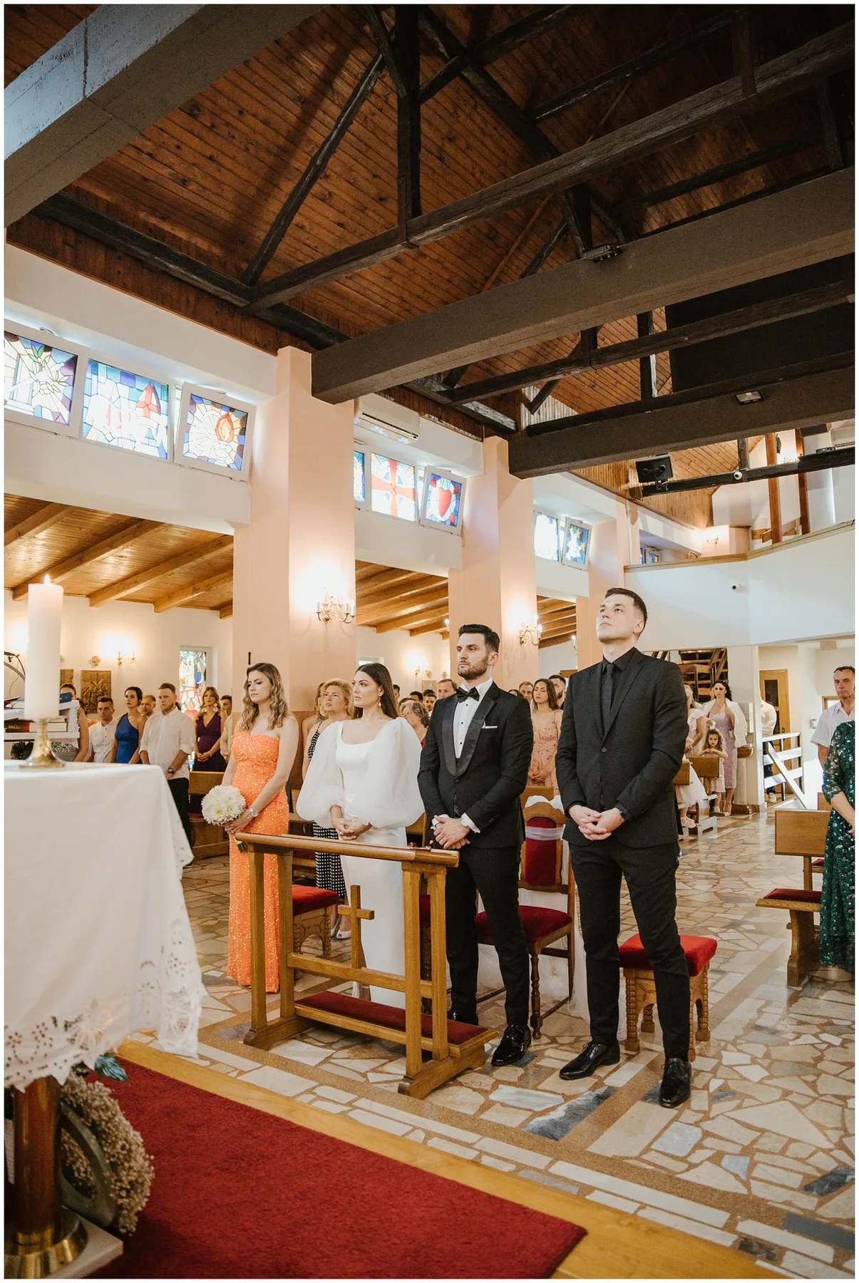 Mladenci i kumovi stoje ispred oltara u crkvi, okruženi gostima tijekom vjenčane ceremonije
