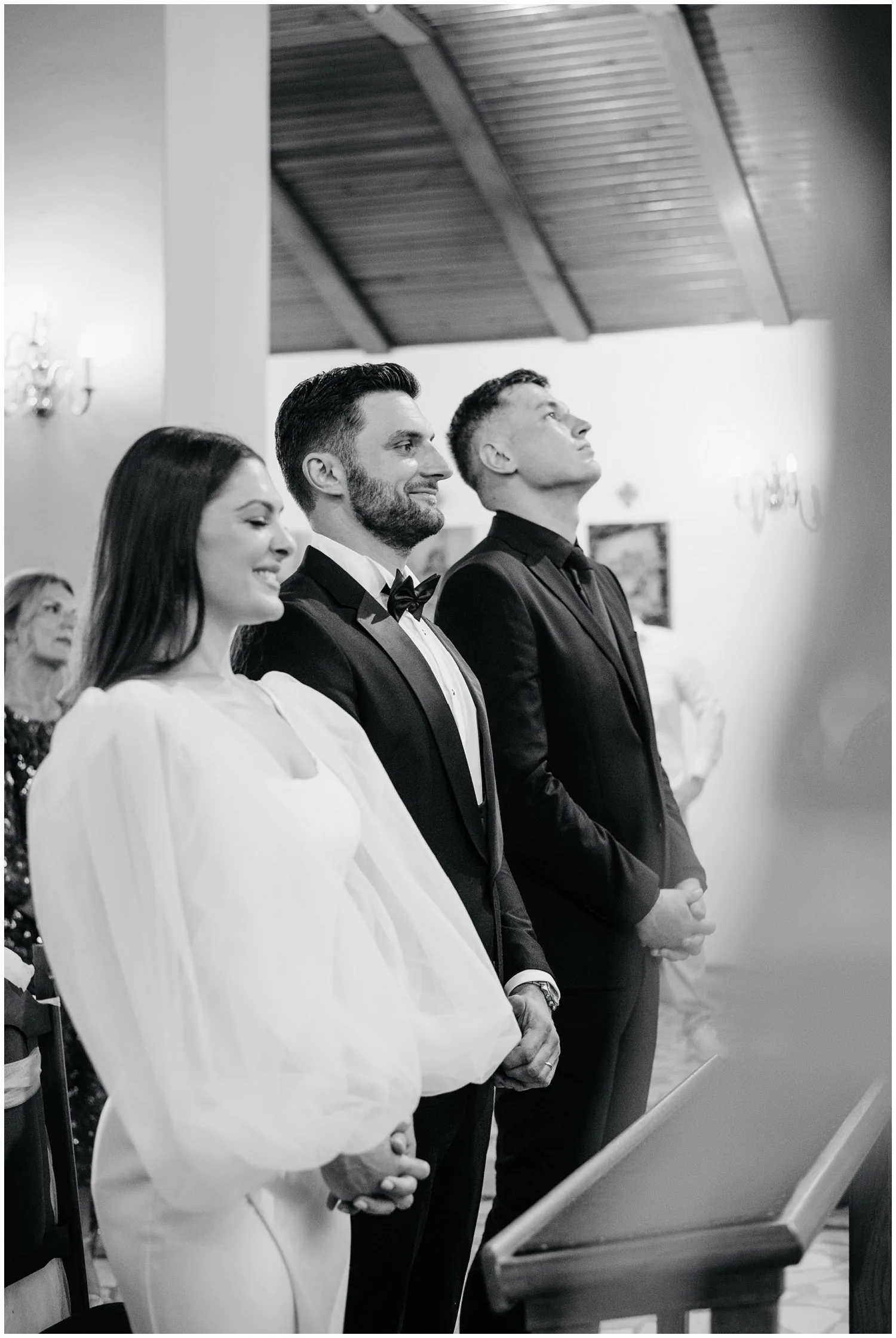Mladenci i kum stoje tijekom vjenčane ceremonije u crkvi, snimljeni iz profila